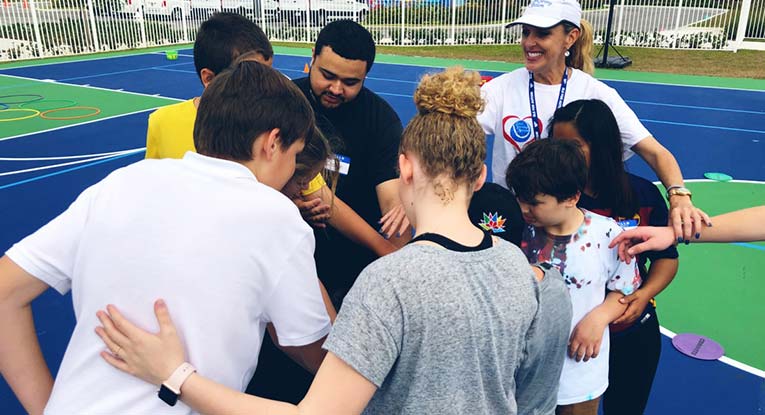 Group of children and coaches cheering at an Els for Autism tennis event hosted by Love Serving Autism