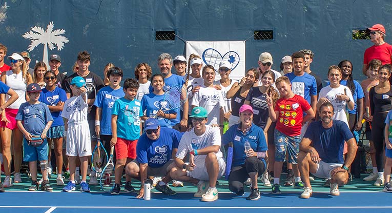 Child with autism holding a tennis racket and smiling during a Love Serving Autism tennis program