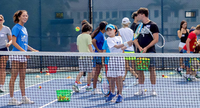 Coach helping children with autism play tennis during a Love Serving Autism session